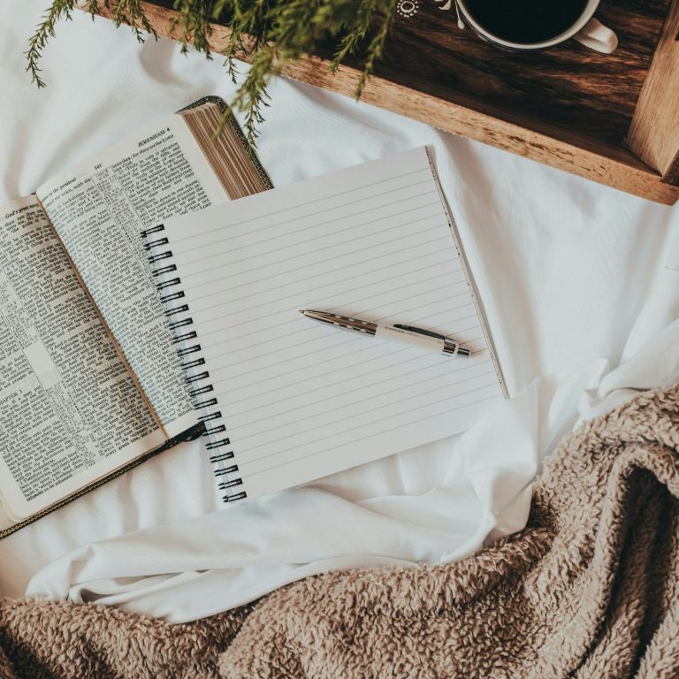 Open book, blank notebook, pen, and a cup on a cozy blanket.
Photo credit: @sixteenmilesoututm on Unsplash