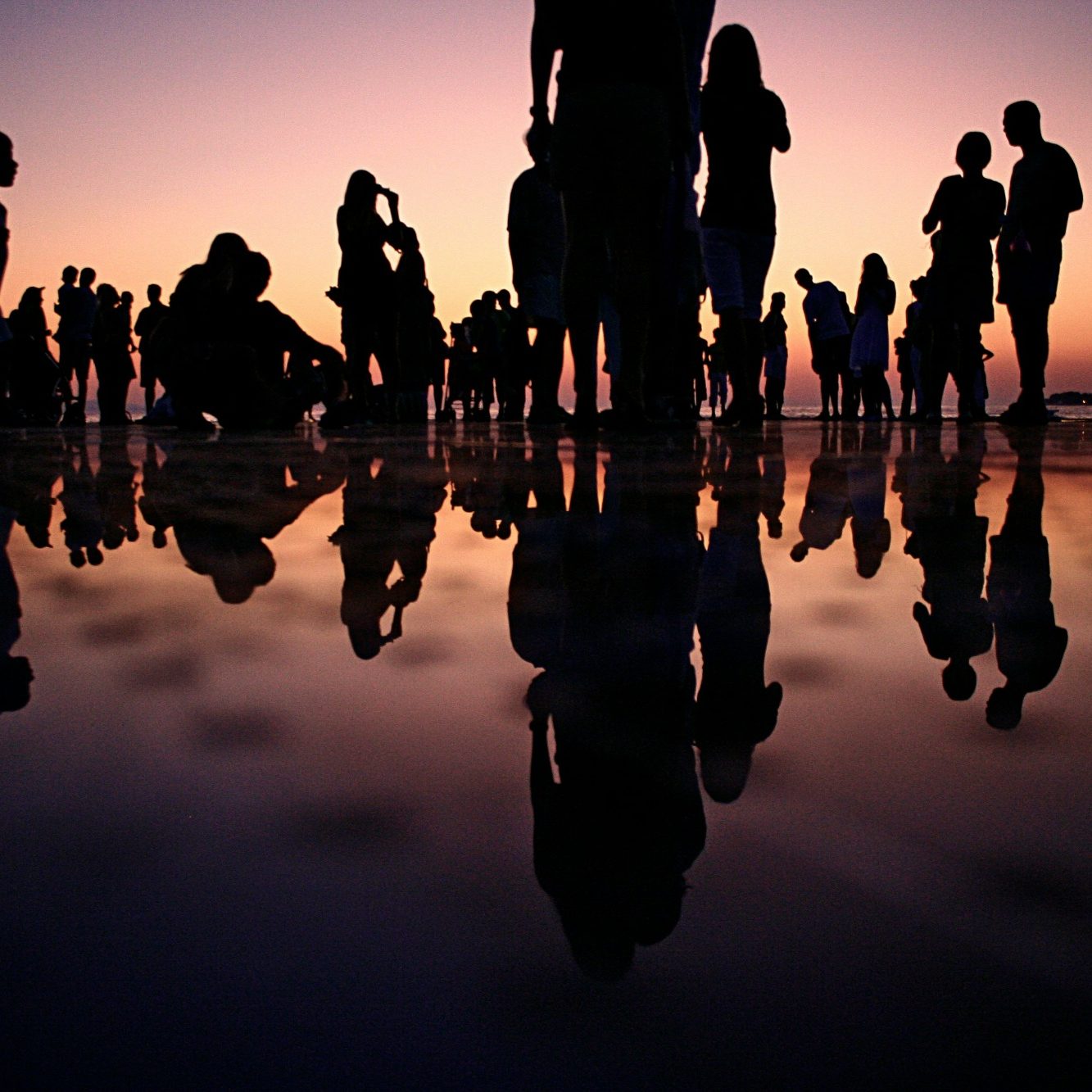 Silhouetted figures against a colorful sunset, reflected in water below.